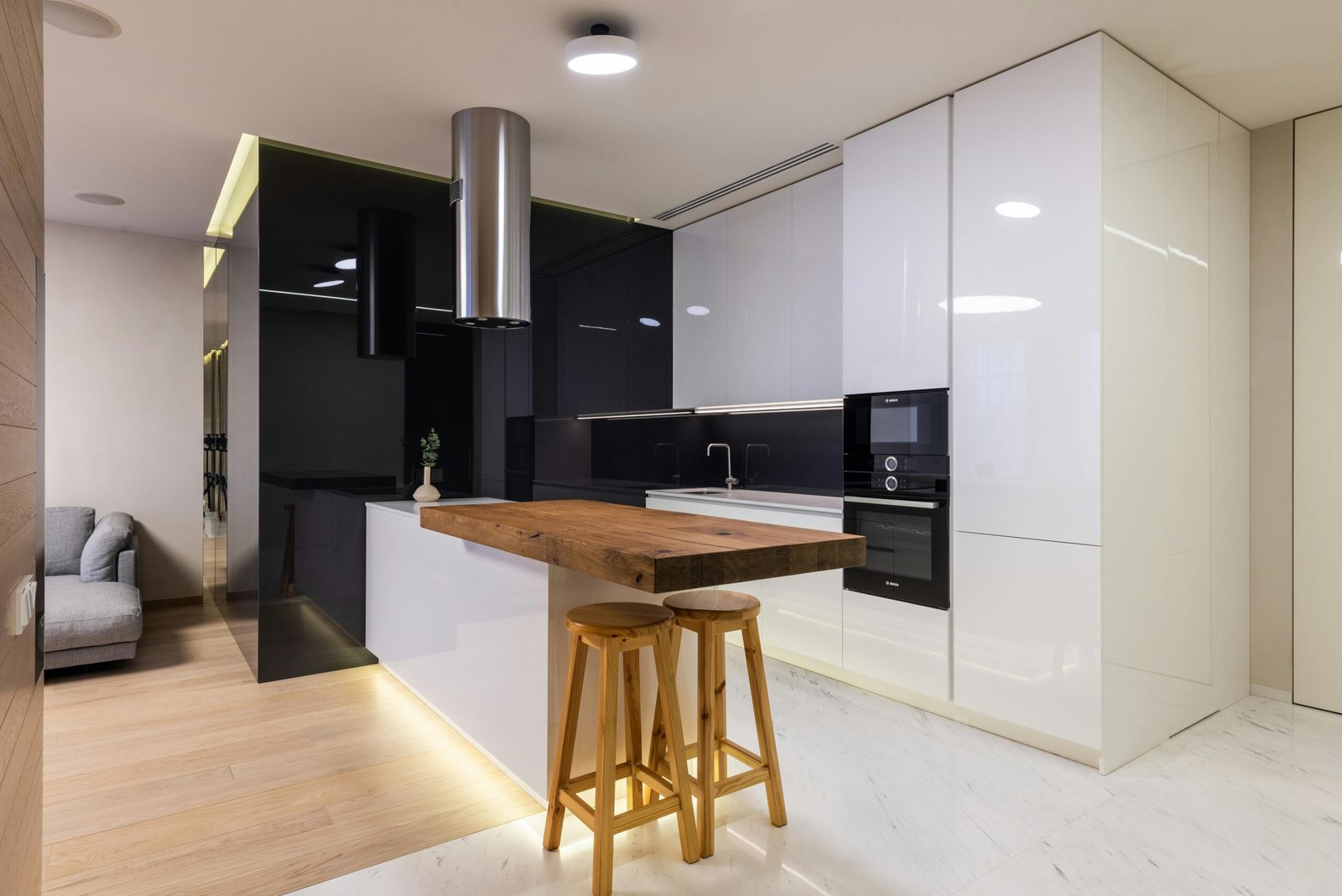 Interior of modern apartment with kitchen zone furnished with glossy cabinets and living area with sofa